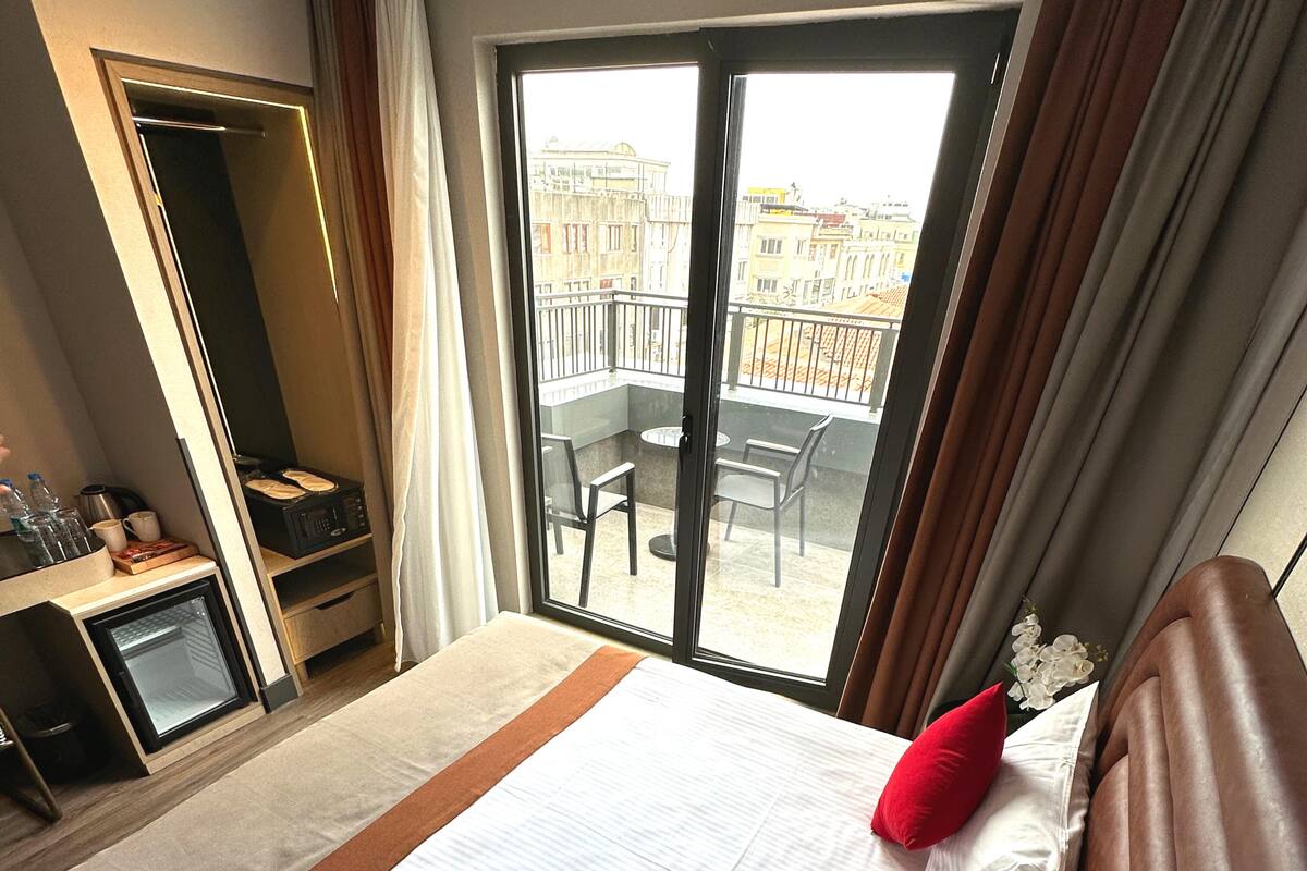 Une chambre d’hôtel comprenant un lit, un bureau avec un ordinateur, un petit réfrigérateur et un balcon avec une table et des chaises.