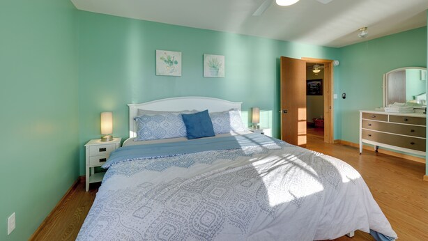 A bedroom with a bed, bedside tables, a ceiling fan, and artwork on the wall. - Honeoye Lake House w/ Community Amenities! (Honeoye)