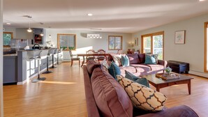 A spacious living area with a large sofa, a dining table, and a kitchen area with modern appliances. - Honeoye Lake House w/ Community Amenities! (Honeoye)