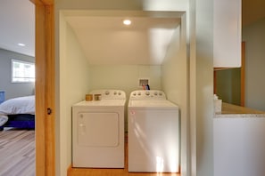 Un cuarto de lavandería con dos lavadoras blancas, una puerta de madera y una ventana con persianas.