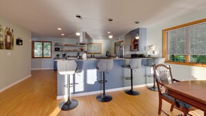 A modern kitchen with bar stools, a dining table, and a view of the outdoors. - Honeoye Lake House w/ Community Amenities! (Honeoye)