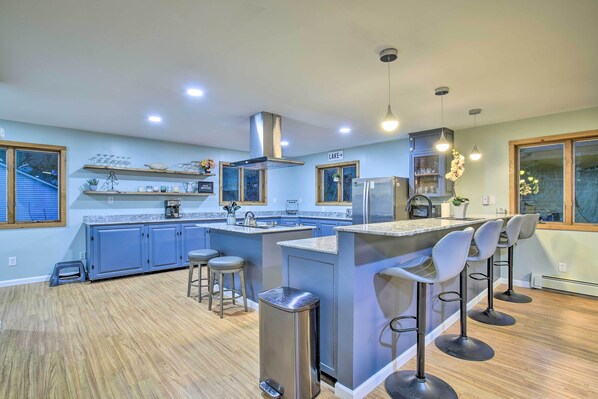 Una cocina moderna con armarios azules, una isla central con taburetes y un bote de basura de acero inoxidable, además de iluminación colgante.