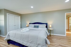 Un lit bien fait, avec une tête de lit bleue, une lampe de chevet et un coussin orné de l’inscription « Bienvenue chez nous ».
