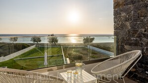 A balcony with a glass railing overlooking a sunset view of the sea. There are two white wicker chairs and a small table with a pitcher and glasses. - Villa Pelagia - Sea Front Villa Pelagia (Sfakia)