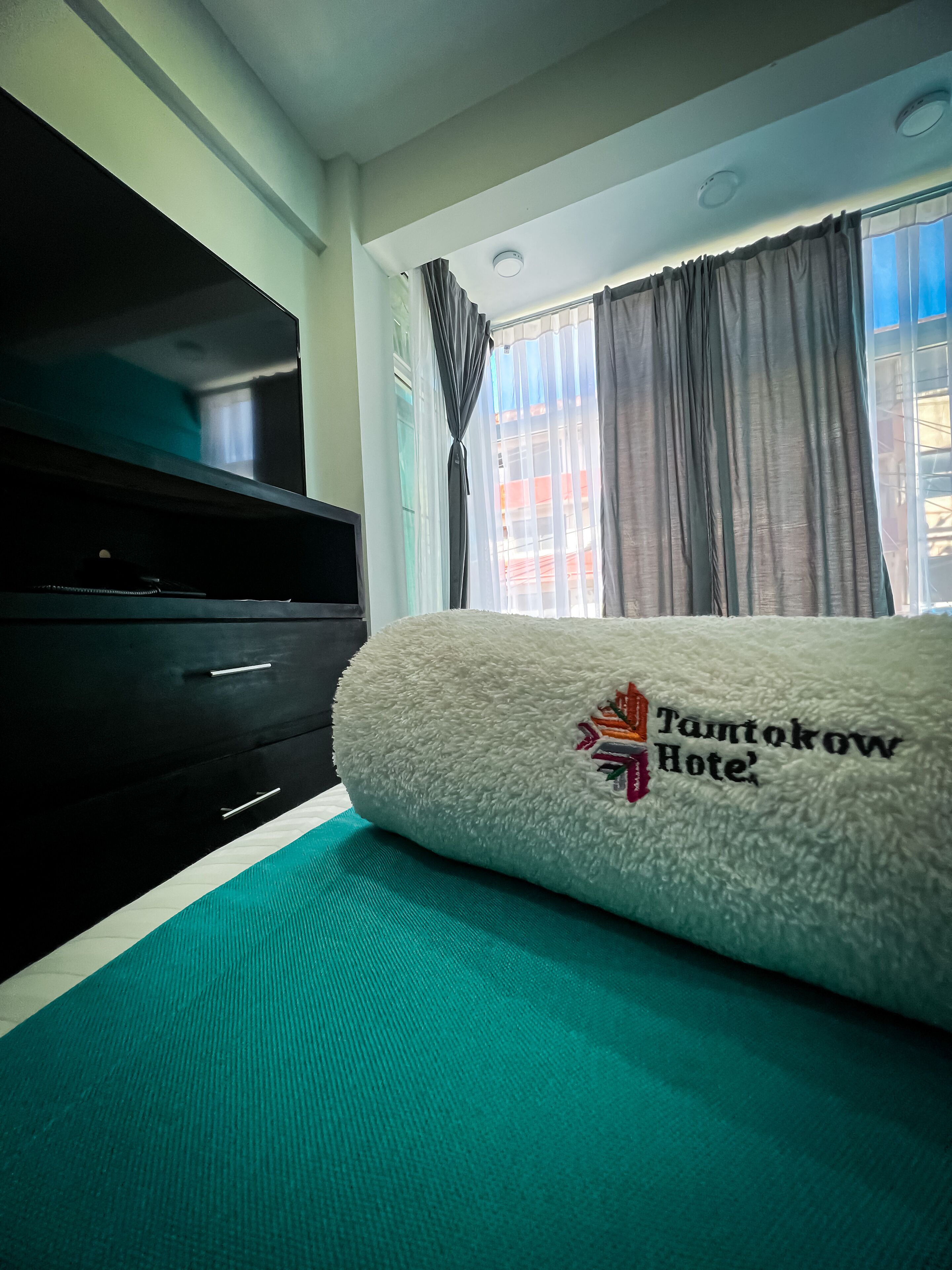 Una habitación de hotel con cama, televisión y ventana con cortinas.