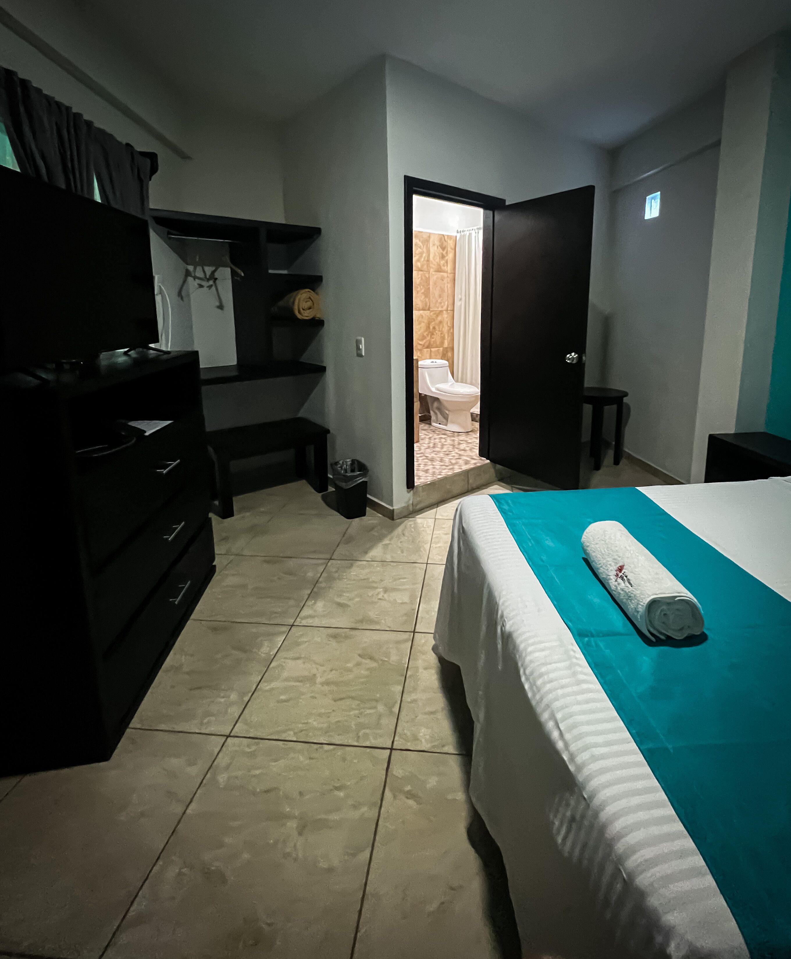 Une chambre d’hôtel comprenant un lit, une commode, une télévision, une petite table et une porte donnant accès à une salle de bain.