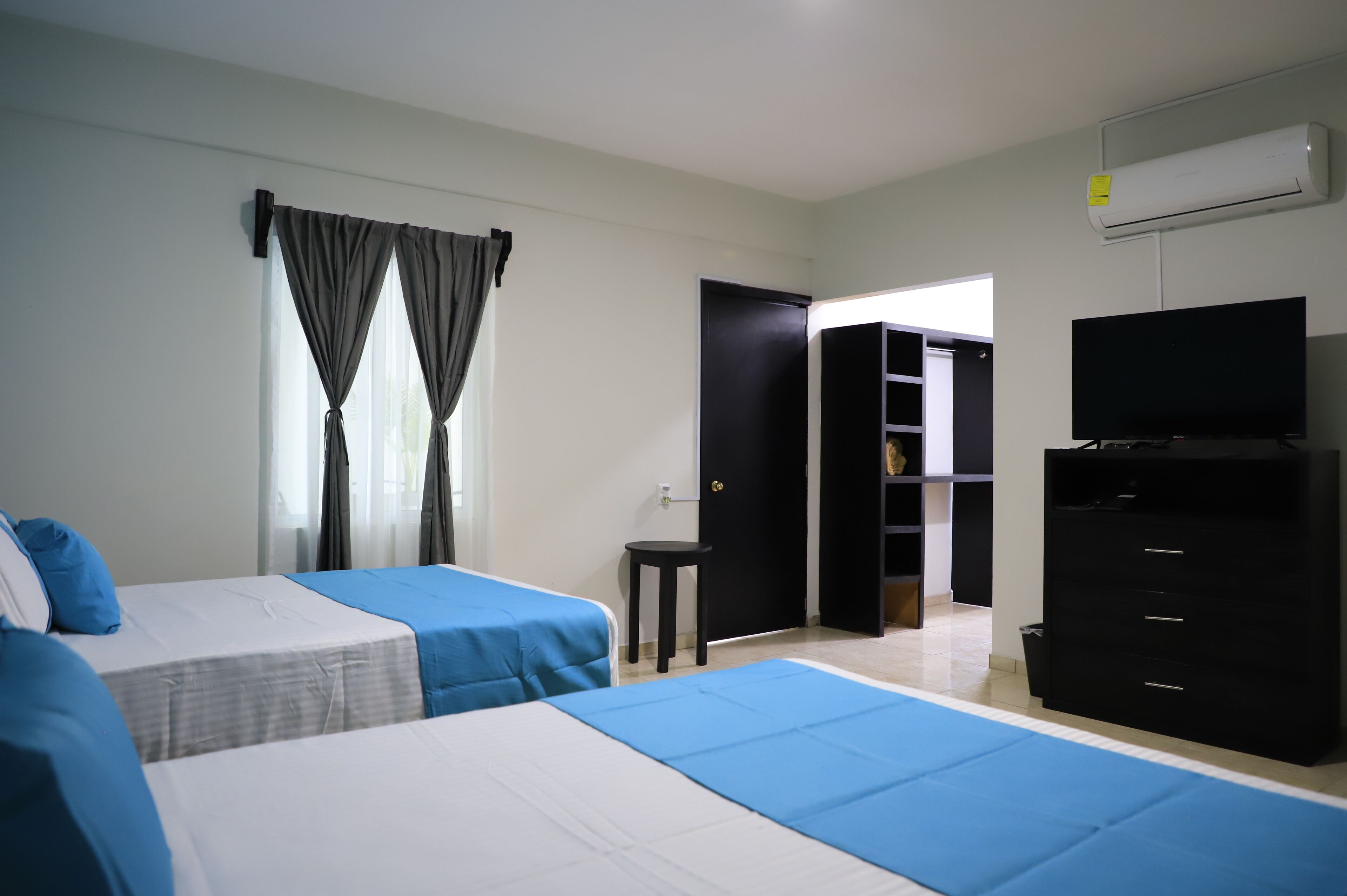 A hotel room with two beds, a TV, a wardrobe, and a door leading to another room.