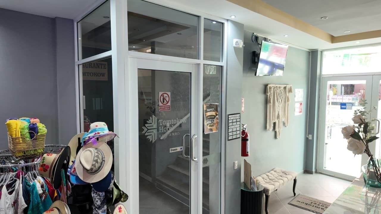 A hotel entrance with a glass door, a small seating area, and a display of hats and clothing.