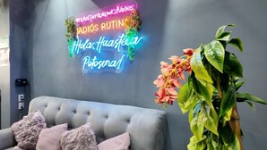 Una habitación moderna con un sofá gris con capitoné, un letrero de neón y una planta en maceta.