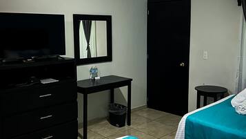 Una habitación de hotel con una cama, televisión, escritorio, cubo de basura y una puerta.