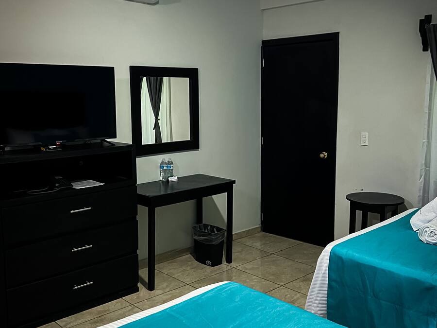 Una habitación de hotel con una cama, televisión, escritorio, cubo de basura y una puerta.