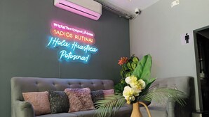 Una sala de estar moderna con un sofá gris, almohadones decorativos, un letrero de neón y un cartel con la palabra 'Relax' sobre una mesa.