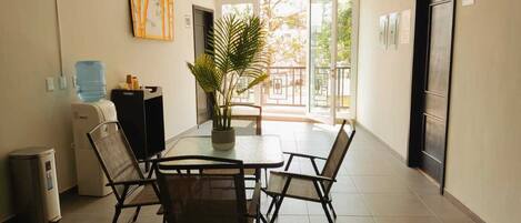 Une chambre d’hôtel équipée d’une table à manger, de chaises, d’un ventilateur de plafond, d’un distributeur d’eau, d’une poubelle et d’une plante en pot.
