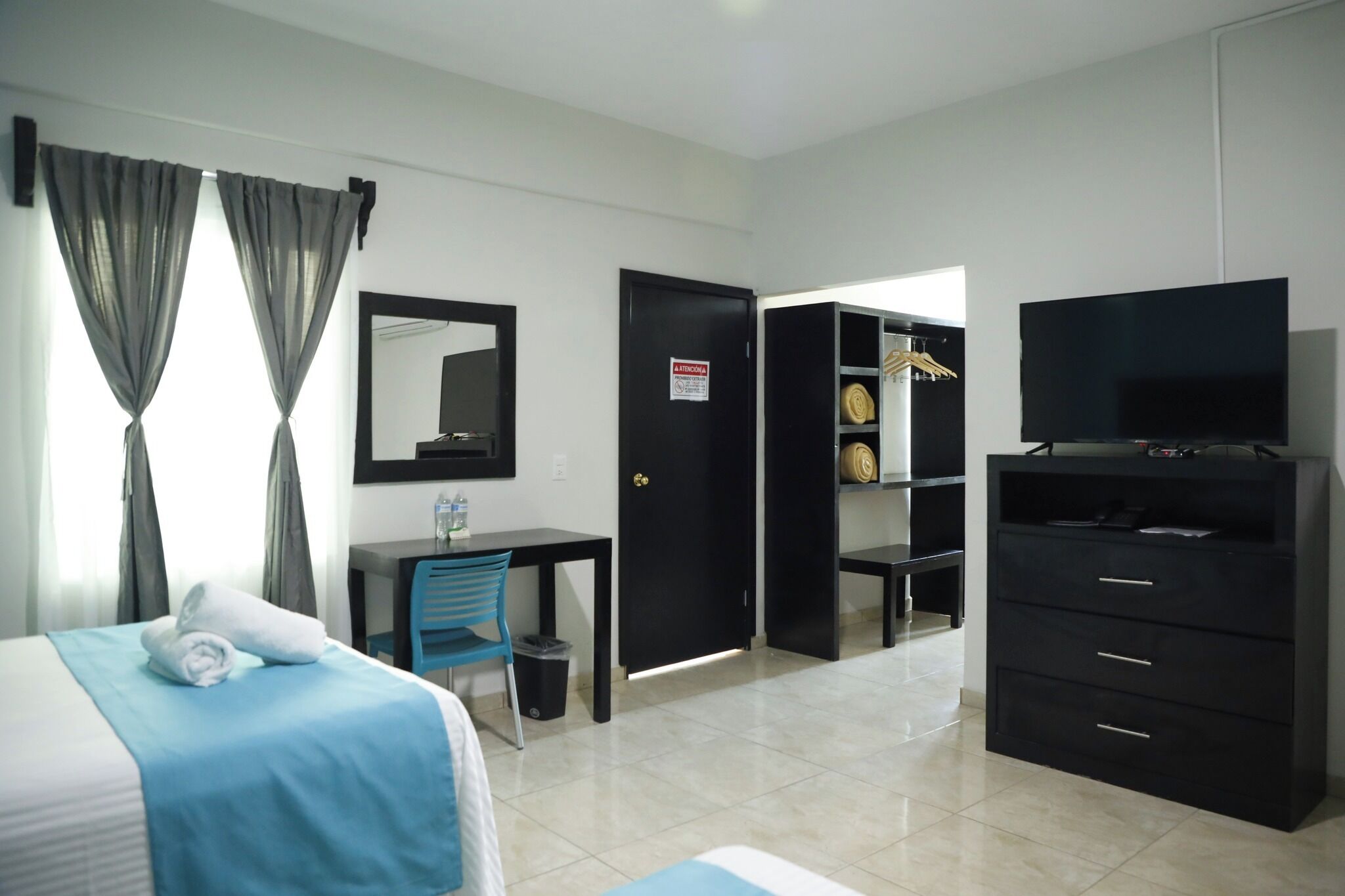 A hotel room with a bed, a desk, a chair, a TV, a wardrobe, and a mirror.