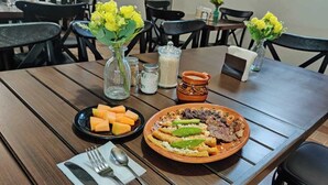 Una mesa de madera con un plato de comida, un bol de fruta y un jarrón con flores amarillas.