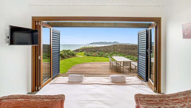 Quarto com uma cama grande, duas toalhas e uma televisão na parede. Possui vista para um deck e área gramada com montanhas ao longe.