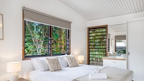 Quarto moderno com uma cama grande, janela com vista para vegetação, mesa de cabeceira com luminária e um espelho.