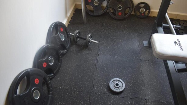 Un gimnasio con una banca, mancuernas y discos de pesas.