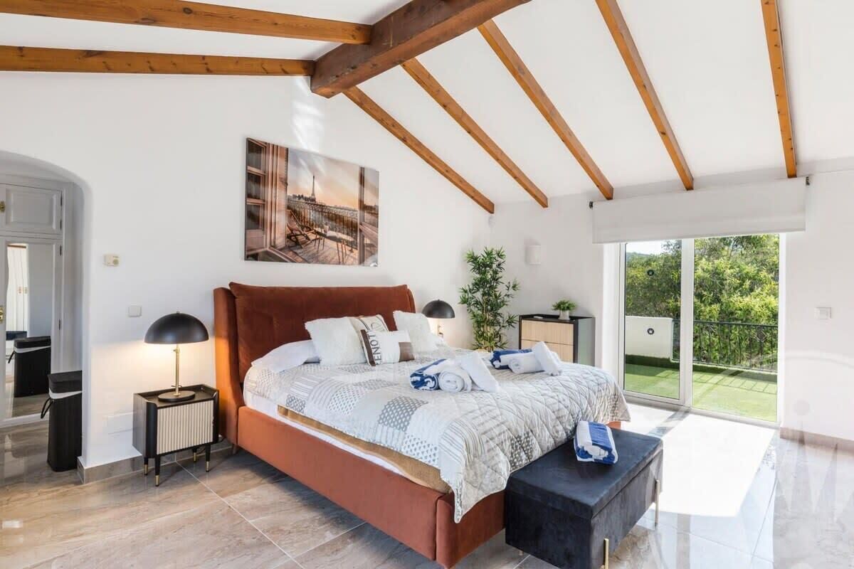 Een slaapkamer met een bed, nachtkastjes, een raam en uitzicht op groen.