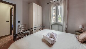 A bedroom with a bed, a wardrobe, a window with curtains, a radiator, and a bedside table with a lamp. - Boboli Guest House Centro Storico Fiorentino (Firenze)
