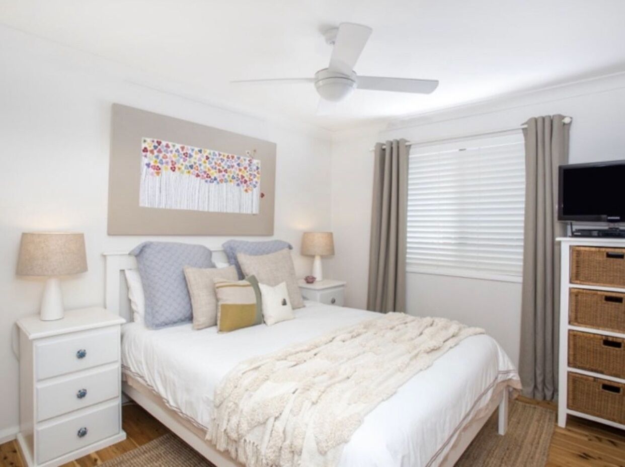 A bedroom with a bed, nightstands, a ceiling fan, a TV, and a window with curtains.
