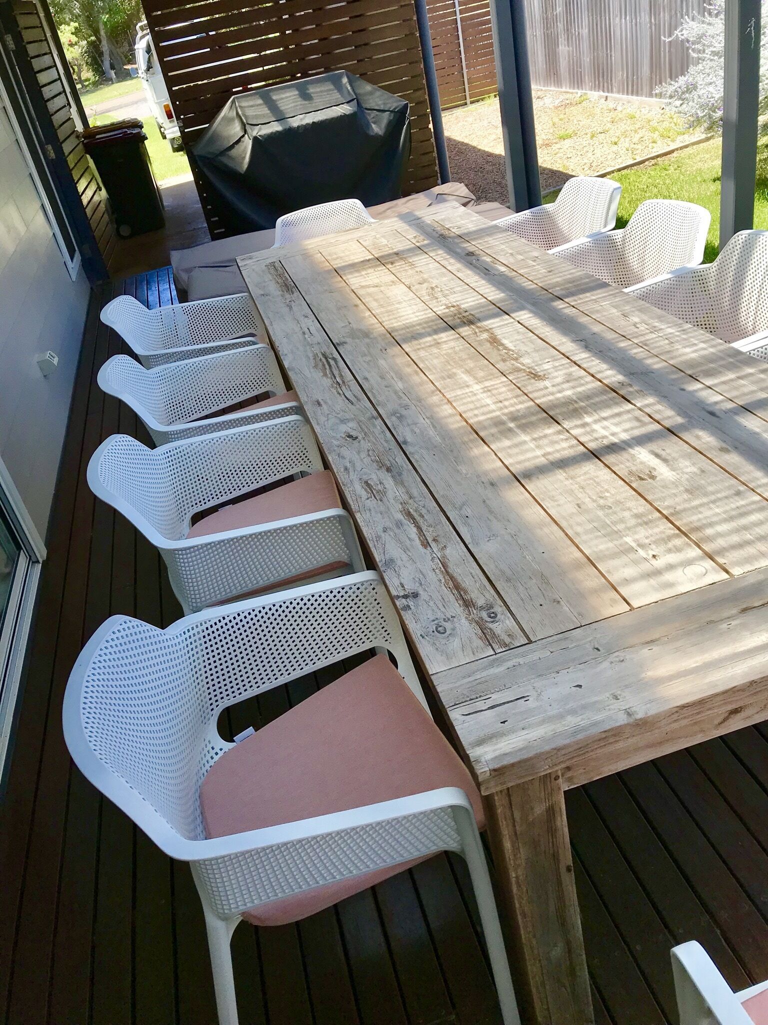 A wooden deck with a large table and white plastic chairs.