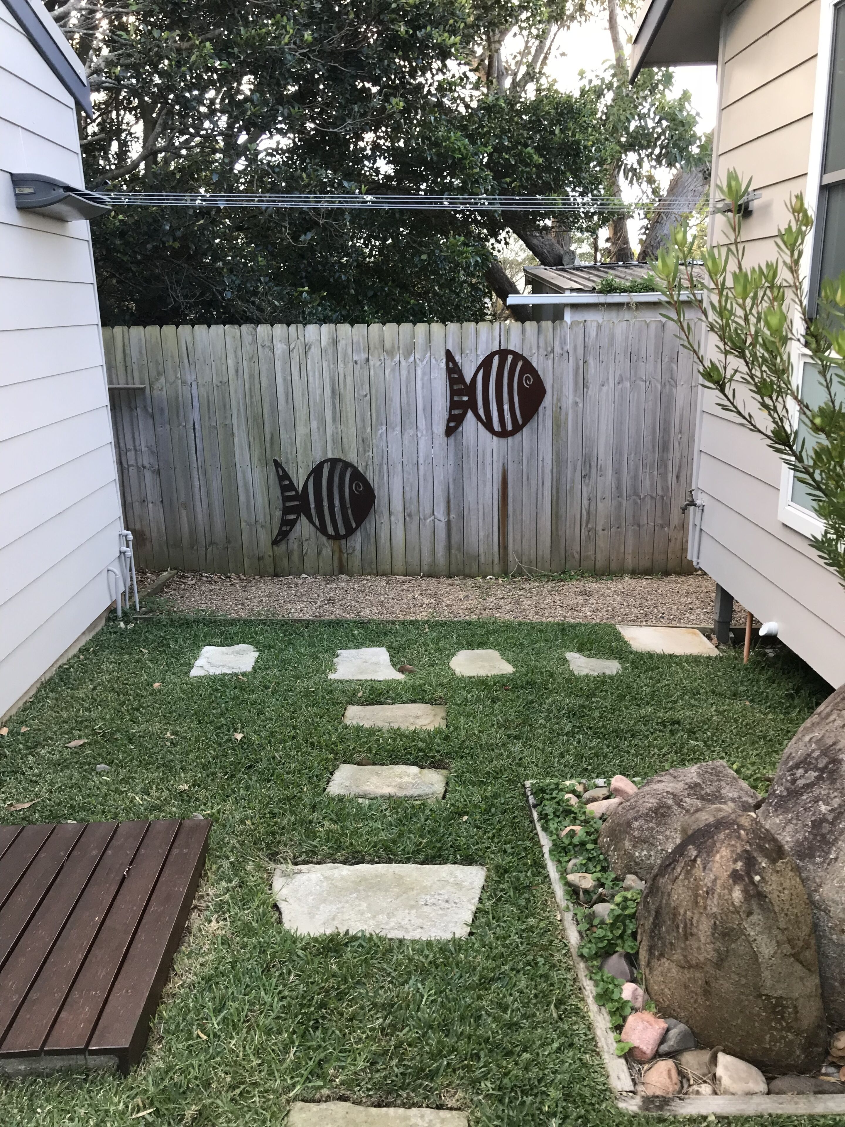 A backyard with a wooden fence, stepping stones, and a wooden deck.