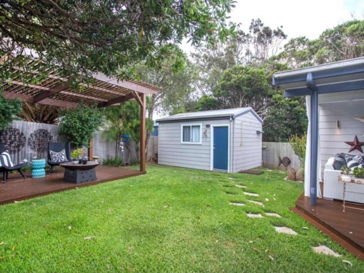 A backyard with a wooden deck, a small shed, and a covered seating area.