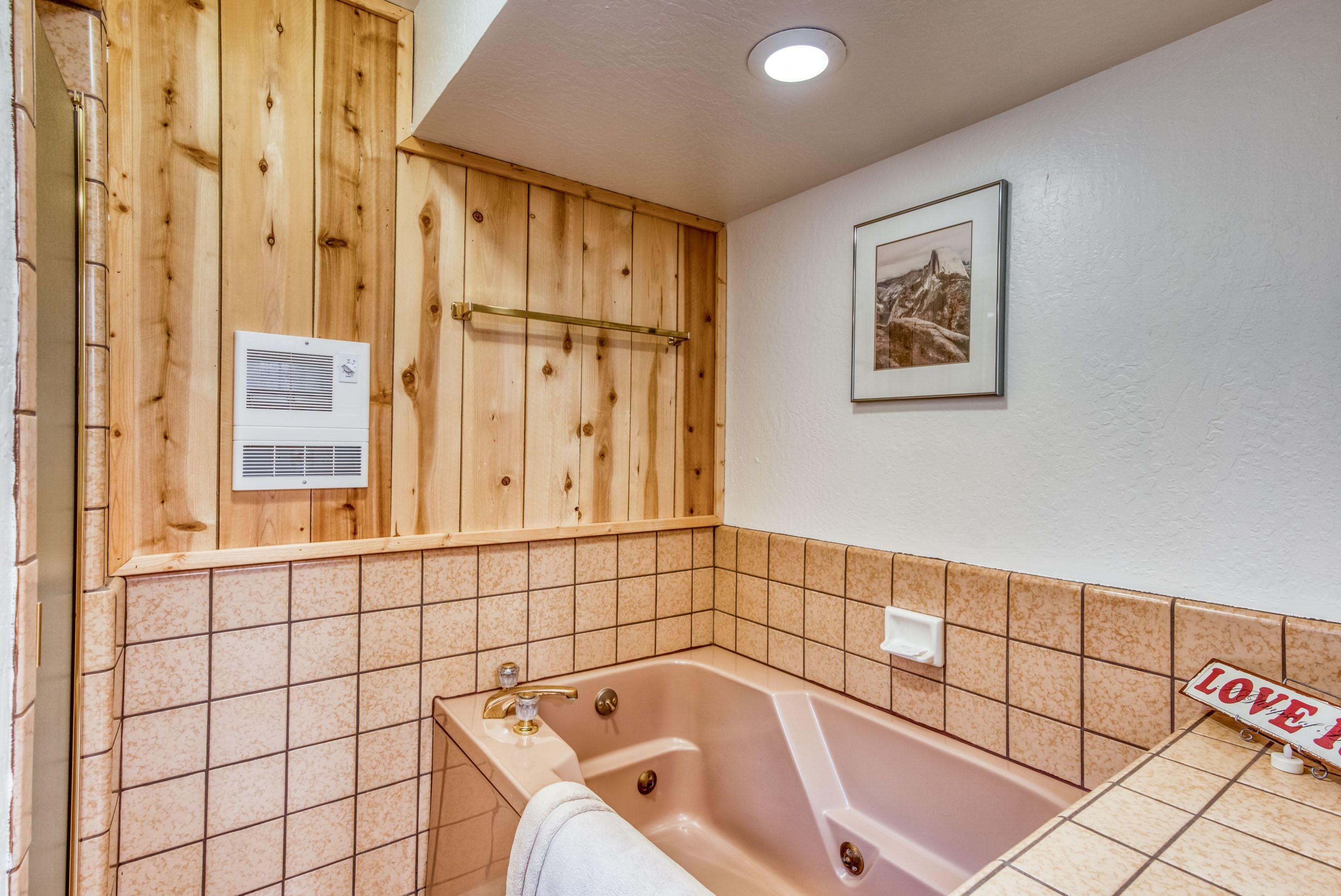 A bathroom with a wooden panel wall, a bathtub, a towel rack, a framed picture, and a 'LOVE' sign.