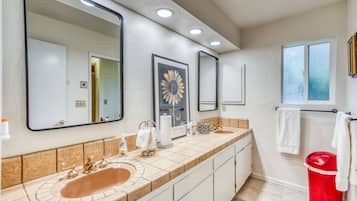 A bathroom with two sinks, a large mirror, and a red trash bin.