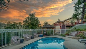 A swimming pool with a white fence, surrounded by wicker chairs and a gazebo. - A Bed of Roses (Oakhurst)