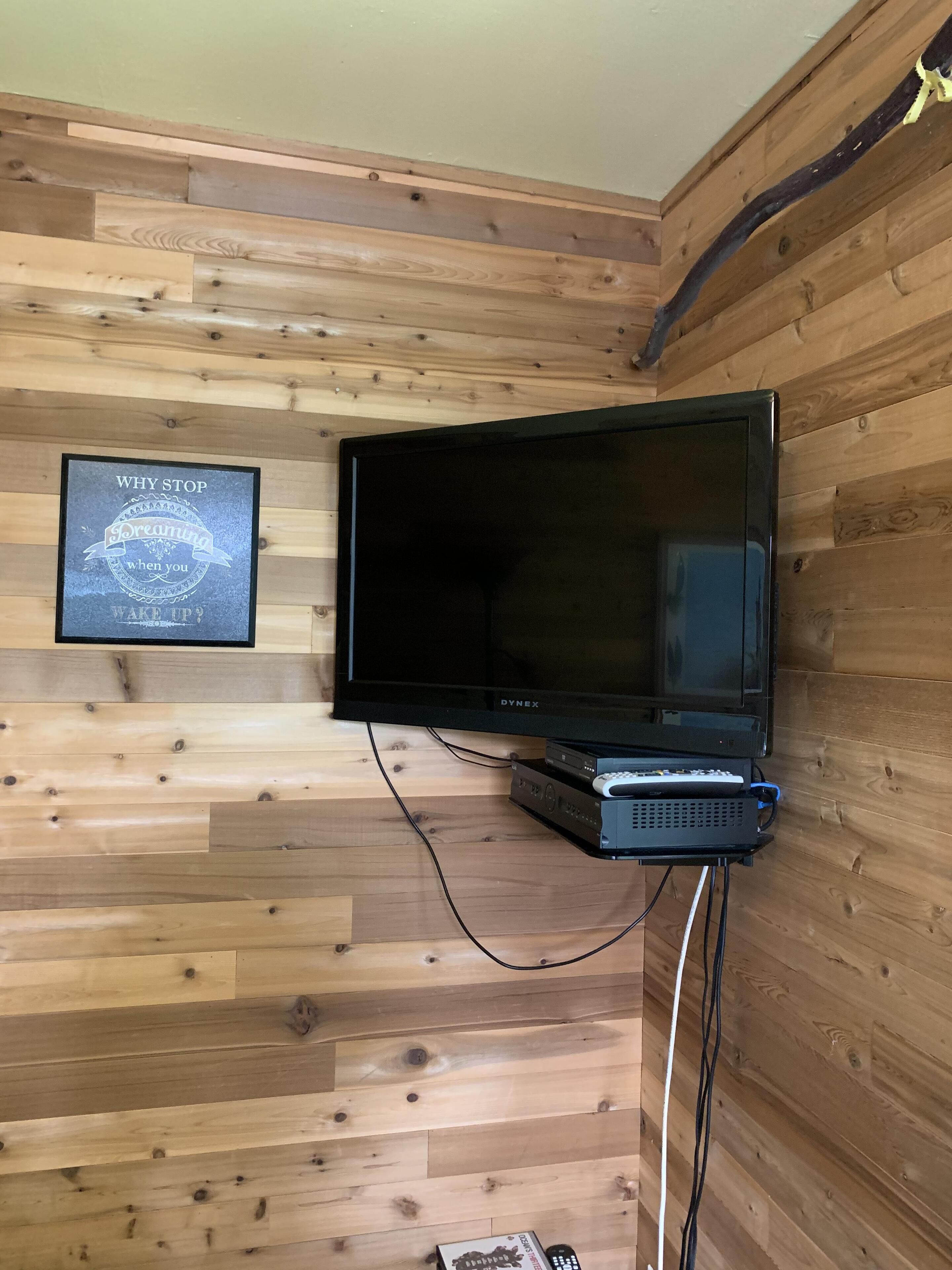 A television mounted on a wooden wall with a framed motivational quote.