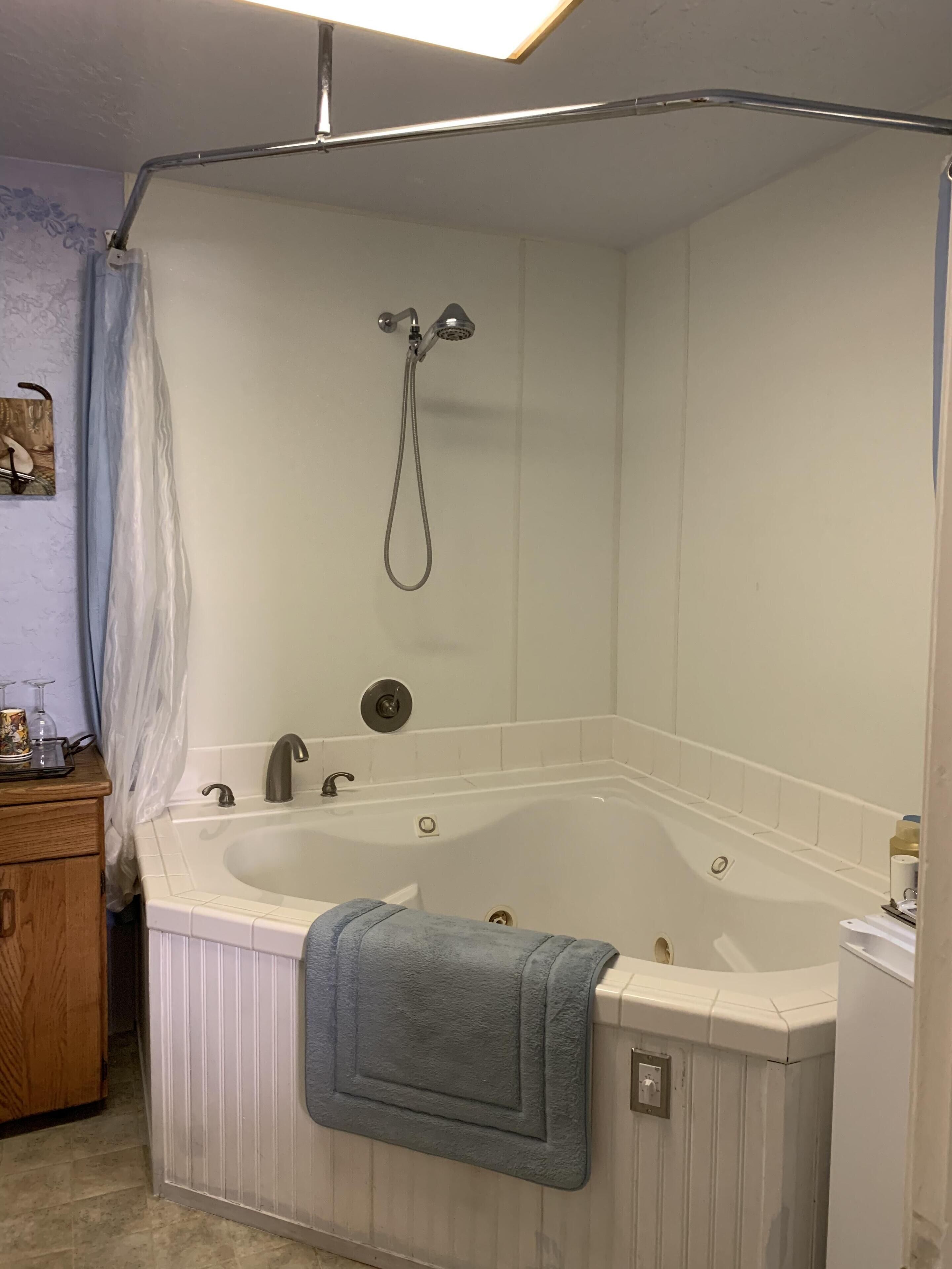 Un baño con una bañera en esquina, un cabezal de ducha y una toalla colgada de la bañera.