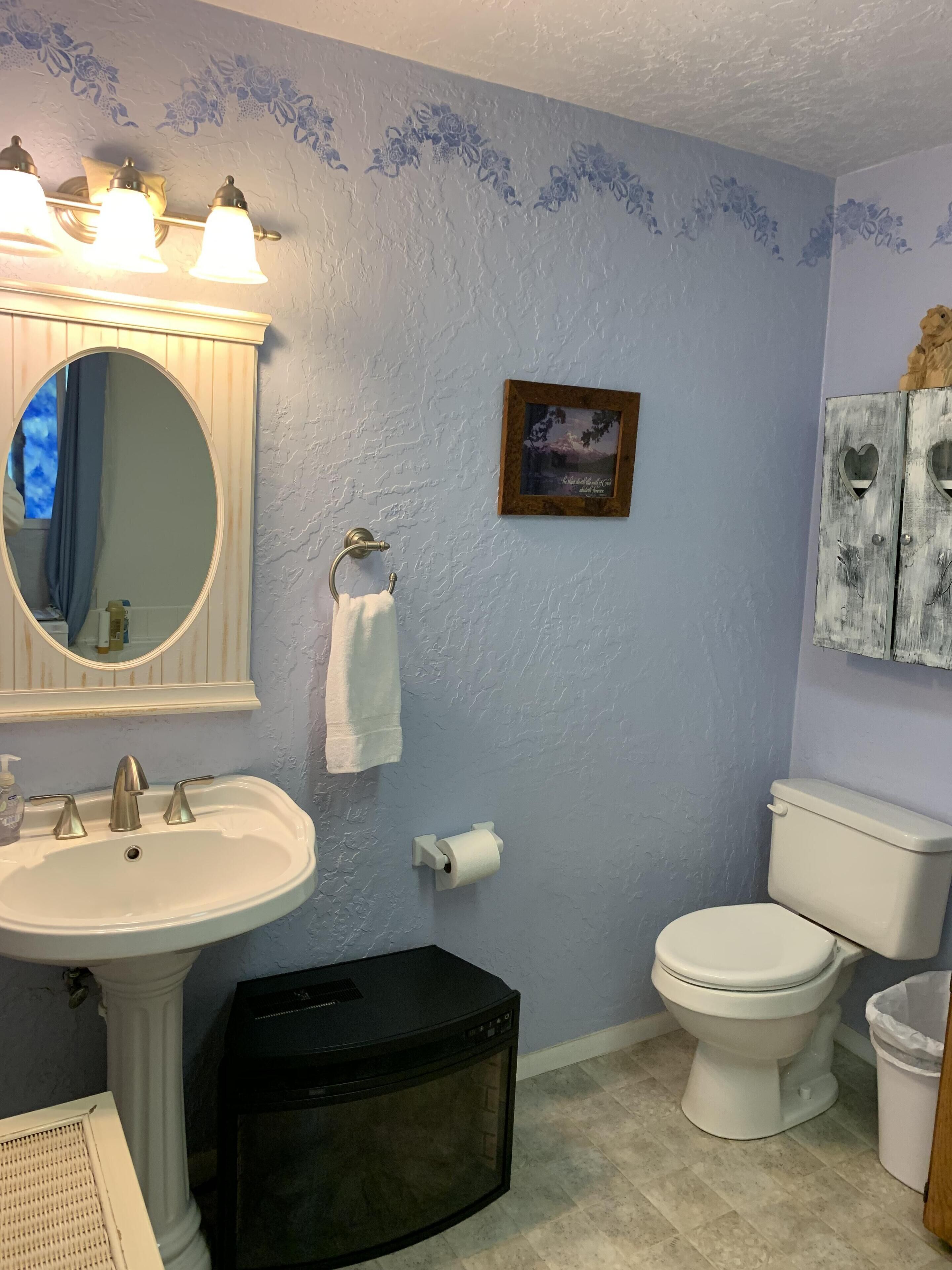 Un baño con lavamanos, espejo, inodoro y un cubo de basura.