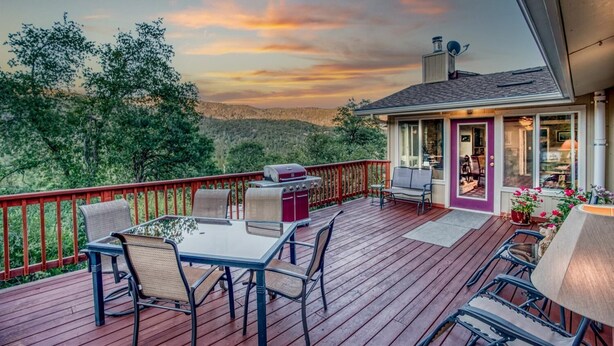 A wooden deck with outdoor furniture, a barbecue grill, and a view of the surrounding landscape. - A Bed of Roses (Oakhurst)