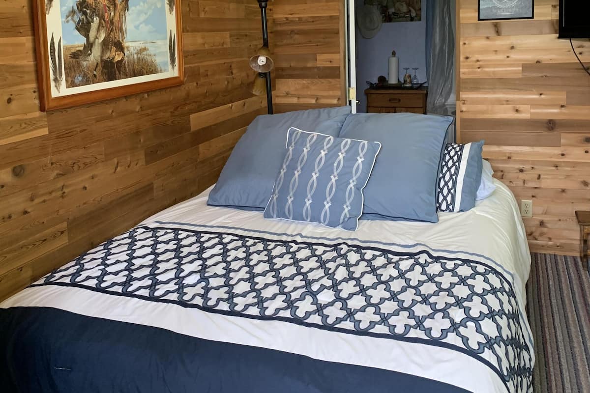 Ein Schlafzimmer mit Holzwand, einem Bett mit gemustertem Überwurf, einem Deckenventilator und einem gerahmten Bild an der Wand.