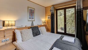 A bedroom with a large bed, wooden headboard, bedside lamps, a framed picture, and a window with curtains. - Apartment Cry - Alpes Agency - Central Chamonix - Sleeps 2-4 (Chamonix-Mont-Blanc)
