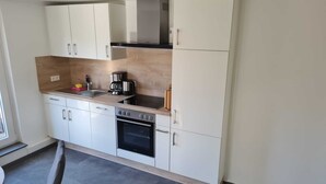 A modern kitchen with white cabinets, a stainless steel range hood, a built-in oven, and a coffee maker. - Ferienwohnung 9 & 40 (Stedesdorf)
