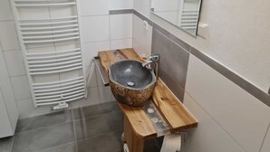 A bathroom with a stone sink on a wooden stand, white tiled walls, and a white radiator. - Ferienwohnung 9 & 40 (Stedesdorf)