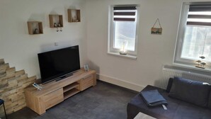 A modern living room with a flat-screen TV on a wooden TV stand, a dark-colored sofa, and a small table with a decorative item. - Ferienwohnung 9 & 40 (Stedesdorf)