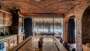A spacious room with a large dining table, wooden cabinets, and a view of a beach through large windows. - La Rosa del Encanto Beachfront Ground Floor West (Playa Encanto)