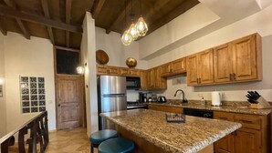 Una cocina con armarios de madera, un refrigerador de acero inoxidable, encimeras de granito y taburetes de bar azules.