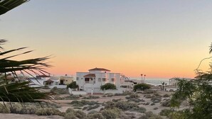 Una propiedad costera con un edificio blanco destacado, rodeada de vegetación desértica y una playa al fondo.