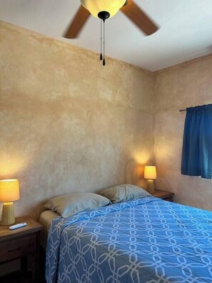 A bedroom with a bed, two bedside lamps, a ceiling fan, and a window with curtains.