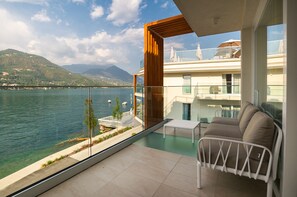 Ein Balkon mit Blick auf einen See und Berge, ein weißer Stuhl und ein Glasgeländer.