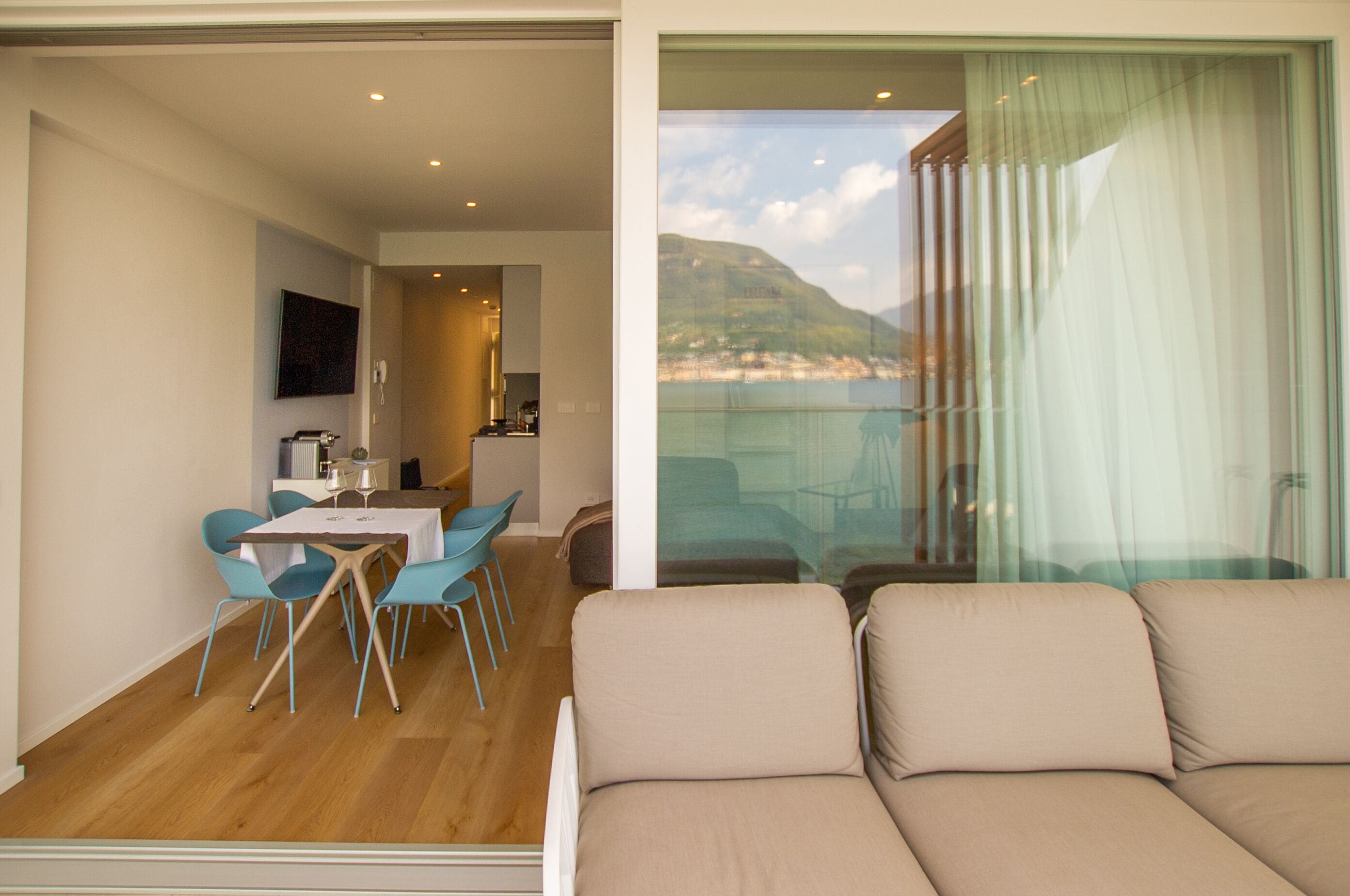 Een modern interieur met een eethoek, een bank en een balkon met uitzicht op een strand en bergen.