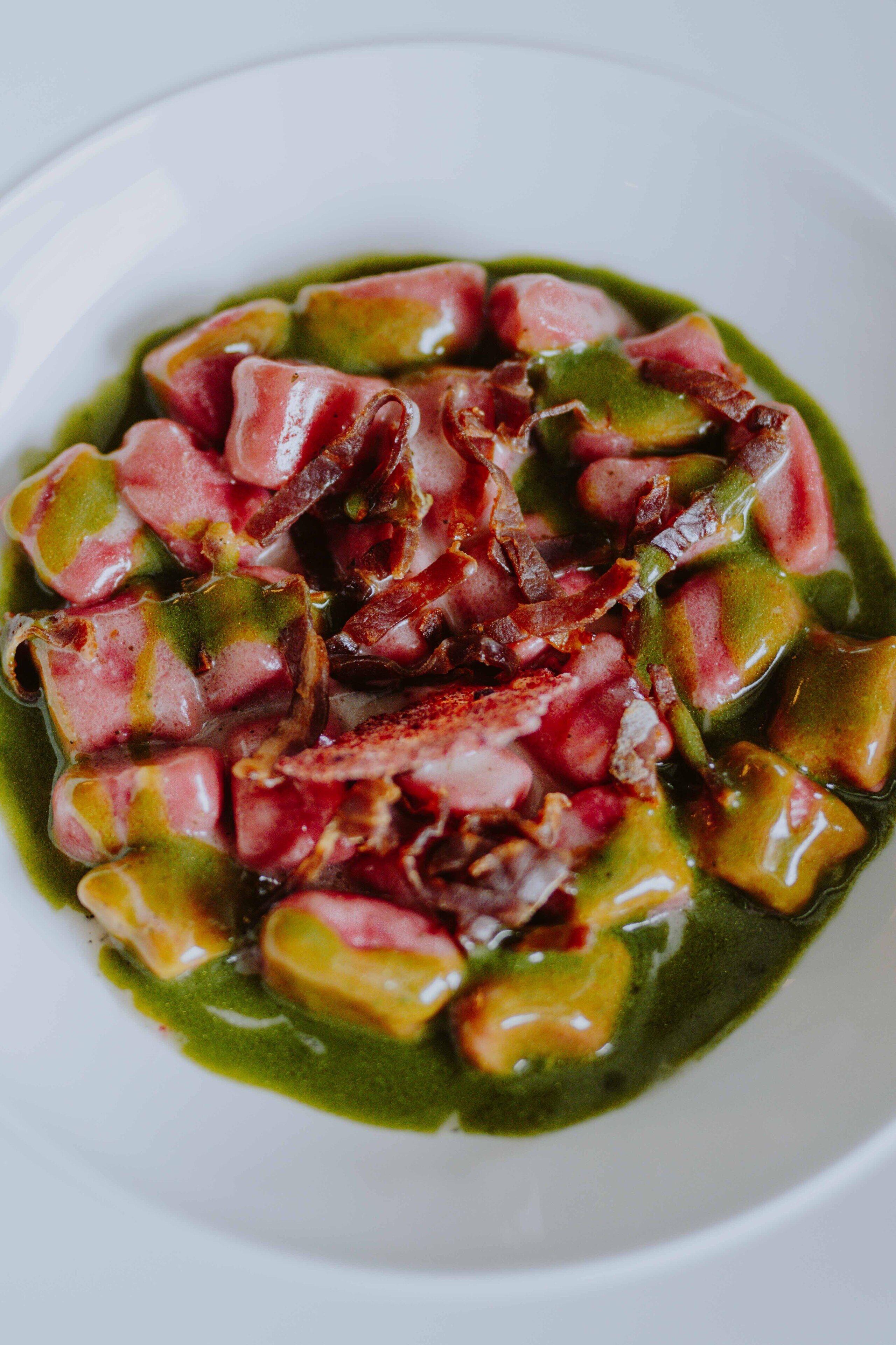 A bowl of food with green sauce and pieces of meat.