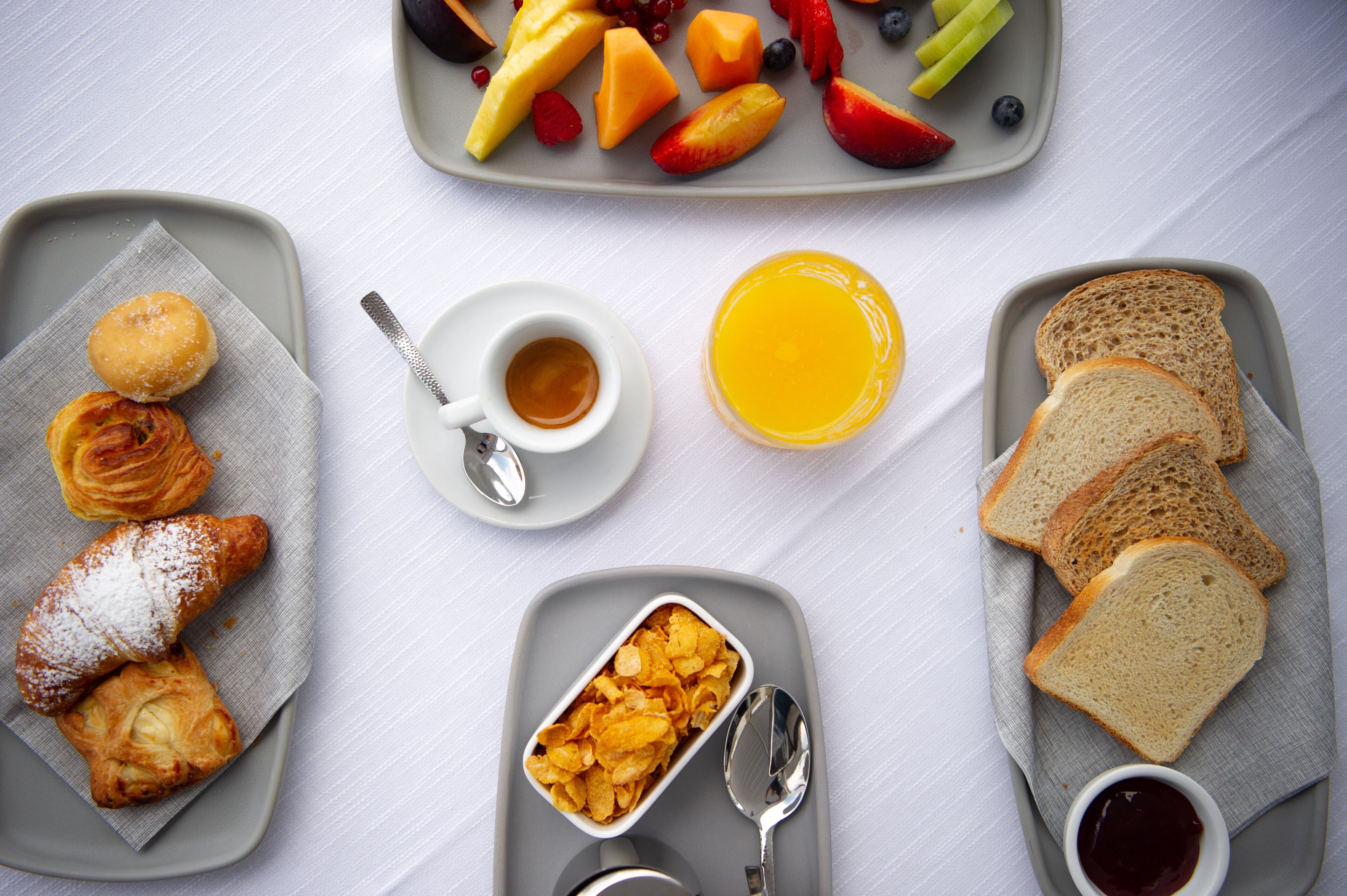 A breakfast setting with croissants, fruit, toast, and beverages on a table.