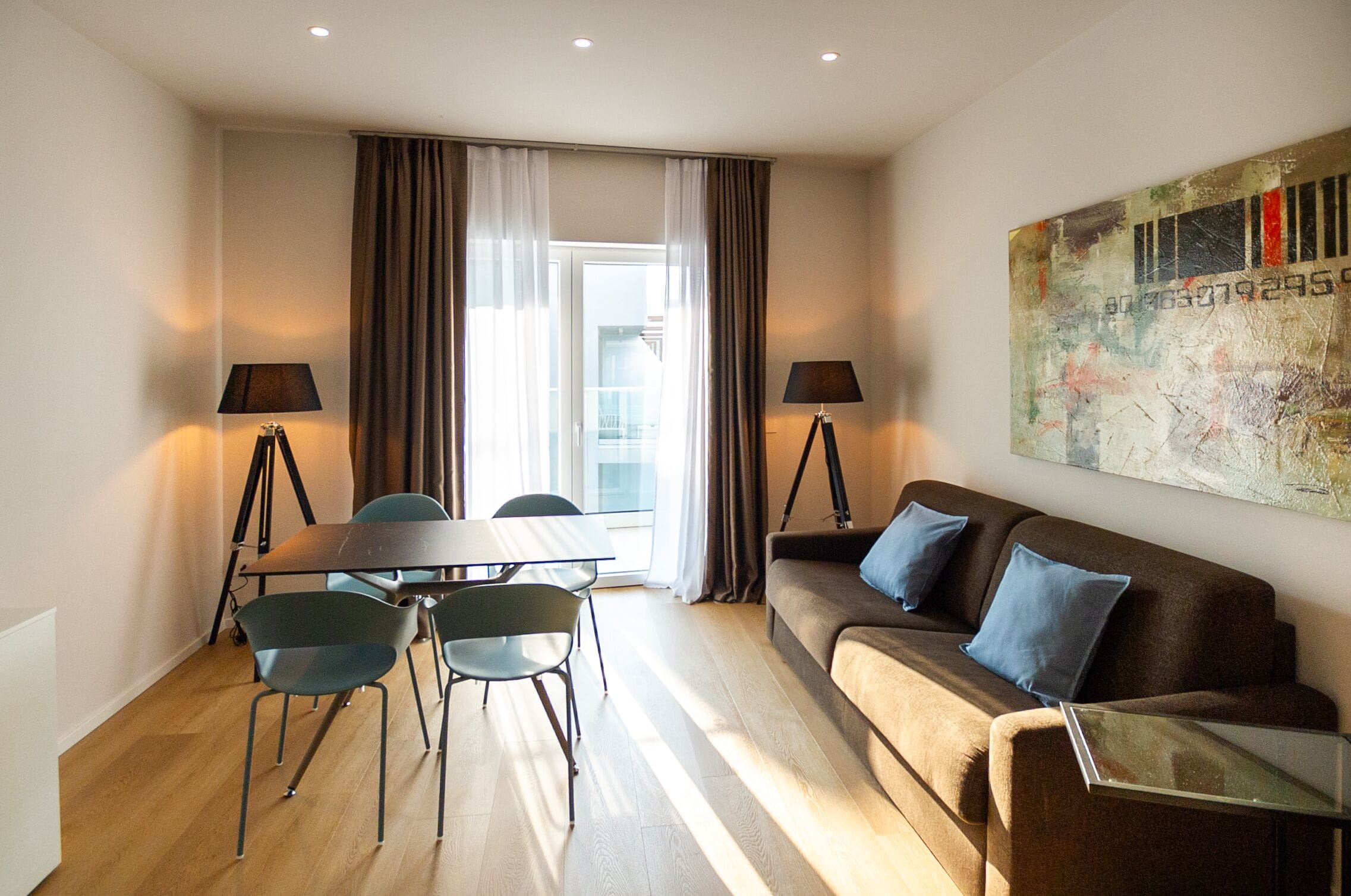 A modern living room with a sofa, a glass coffee table, a dining table with chairs, and two floor lamps.