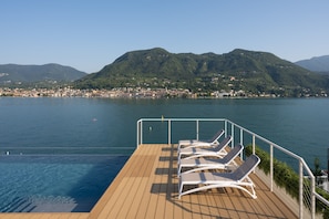 Una terrazza con poltrone relax che si affaccia su un lago e una cittadina sullo sfondo.